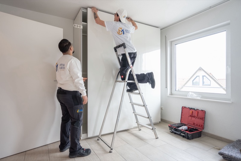 Zwei Mitarbeiter bauen in der neuen Wohnung einen Kleiderschrank auf.