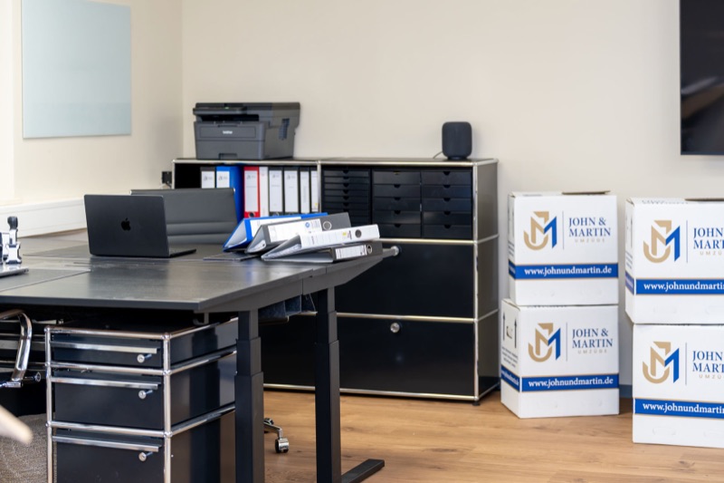 Ein Büro am Umzugstag: Schreibtische, Systemmöbel und gestapelte Umzugskartons von John & Martin.