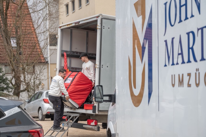 Zwei Mitarbeiter verladen ein verpacktes Möbelstück in den Umzugswagen.