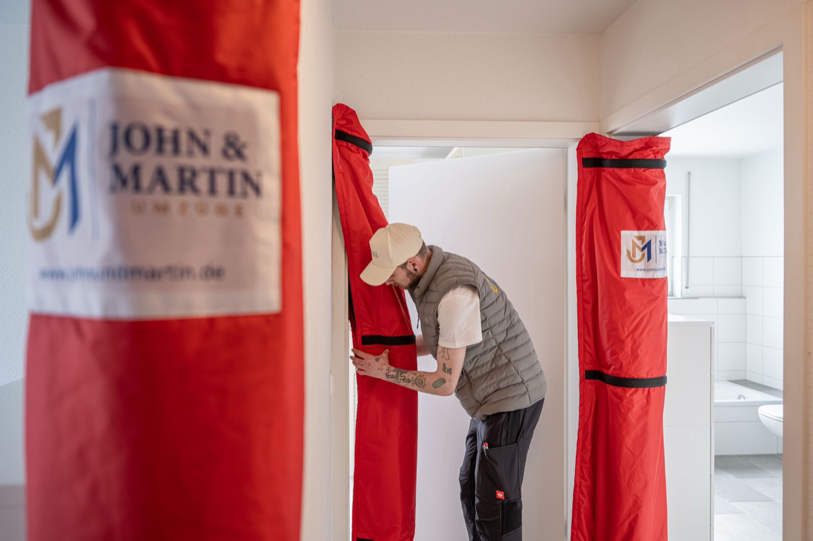 Ein Mitarbeiter von John & Martin bringt roten Türschutz mit Firmenlogo am Türrahmen an.