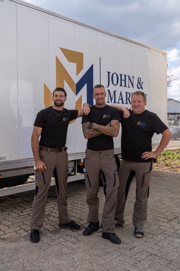 Drei Mitarbeiter von John & Martin stehen vor einem Umzugswagen mit großem Firmenlogo.