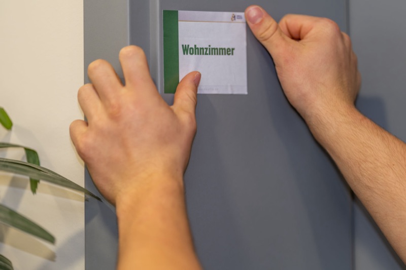 Der passende grüne Aufkleber „Wohnzimmer“ wird an die Türzarge geklebt.