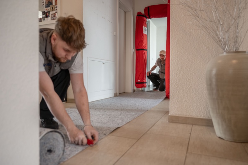 Ein Mitarbeiter rollt Schutzvlies im Flur aus.