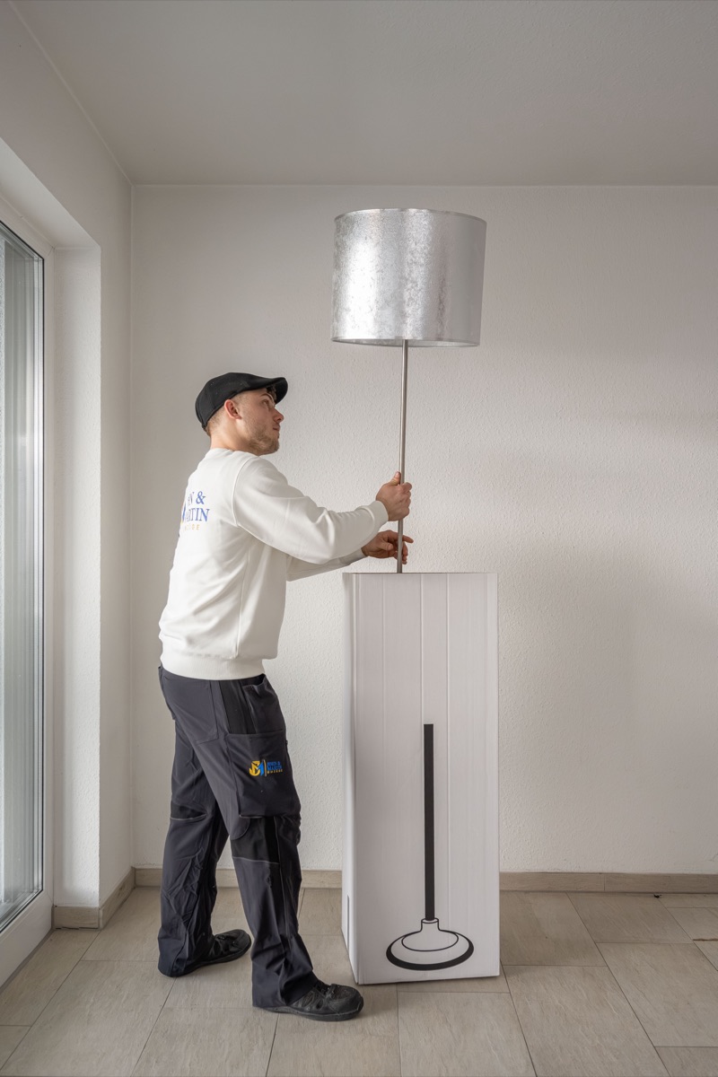 Ein Mitarbeiter stellt eine Stehlampe neben ihren hohen Spezialkarton.